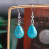 Turquoise teardrop earrings on a wooden stand with a blurred background