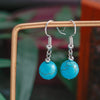 Turquoise earrings with silver hooks on a wooden stand against a blurred natural background