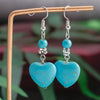 Turquoise heart-shaped earrings on a stand with a blurred green background