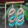 Pair of silver and turquoise beaded earrings on a stand with a green leafy background
