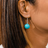 Close-up of an ear wearing a turquoise bead earring with brown hair.