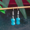 Turquoise glass earrings with silver hooks on a dark background