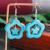 Turquoise flower-shaped earrings with star center on a wooden stand.
