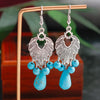 Silver earrings with turquoise beads on a wooden stand.