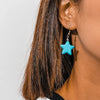 Close-up of a person wearing turquoise star-shaped earrings with a neutral background