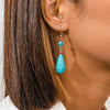 Close-up of a turquoise teardrop earring on an ear with brown hair.