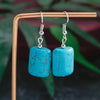 Turquoise earrings on a wooden stand with a blurred green background