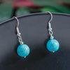 Turquoise bead earrings on a dark surface with a blurred green background