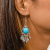 Close-up of an ear wearing a turquoise stone earring with silver detailing.