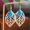 Pair of earrings with blue stones and leaf-like designs on a wooden stand.