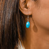 Close-up of an ear wearing a turquoise earring with hair partially obscuring the view.