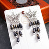 Butterfly earrings with black and gold beads on a white card with 'Handmade' text, against a dark background.