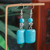 Turquoise earrings with silver accents on a wooden stand against a blurred natural background
