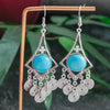 Turquoise stone earrings with silver accents on a stand with a green leafy background