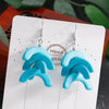 Turquoise wave-shaped earrings on a white card with 'Handmade' text, against a blurred natural background.