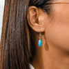 Close-up of an ear wearing a turquoise earring with dark hair.