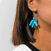 Close-up of a person wearing turquoise earrings with a neutral background
