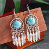 Turquoise stone and silver feather earrings on a wooden stand with 'hippie' text.
