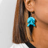 Close-up of a person wearing turquoise earrings with a neutral background