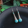 Turquoise earrings with silver loops on a dark surface with green leaves in the background