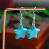 Blue star-shaped earrings on a gold stand with a blurred green and brown background