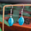 Turquoise earrings with silver hooks on a wooden stand against a blurred natural background