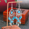 Blue beaded earrings with silver accents on a wooden stand.
