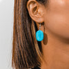 Close-up of a turquoise earring worn by a person with brown hair.