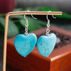 Turquoise heart-shaped earrings on a wooden stand with a blurred natural background