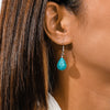 Close-up of a turquoise teardrop earring worn by a person with dark hair.