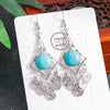 Pair of earrings with turquoise stones and silver detailing on a white card.