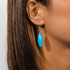 Close-up of an ear wearing a turquoise earring with a neutral background