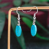 Turquoise bead earrings on a wooden stand with a blurred green background