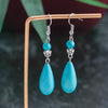 Turquoise teardrop earrings on a wooden stand with a blurred green background