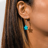 Close-up of an ear wearing a turquoise star-shaped earring with a neutral background
