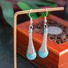 Teardrop-shaped earrings with turquoise beads on a wooden stand.