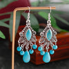 Turquoise teardrop and bead earrings on a wooden stand with a blurred green background