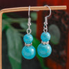 Turquoise bead earrings on a wooden stand with a blurred natural background