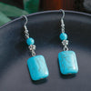 Turquoise earrings with silver hooks on a dark surface