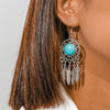Earring with turquoise stone and feather details worn by a person with brown hair.