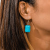 Close-up of an ear wearing a turquoise earring with dark hair.