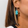 Close-up of a person wearing turquoise beaded earrings with a neutral background