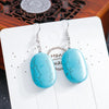 Turquoise earrings on a white card with a decorative background