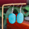 Turquoise earrings on a wooden stand with a blurred natural background