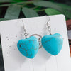 Turquoise heart-shaped earrings on a white card with a blurred green leafy background