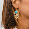 Close-up of a person wearing a gold earring with a blue gemstone.