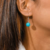 Close-up of an ear wearing a turquoise bead earring with a blurred background