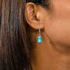 Close-up of an ear wearing a turquoise earring with dark hair.