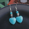 Turquoise heart-shaped earrings with silver hooks on a dark surface