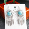 Pair of silver earrings with turquoise stones on a white card.